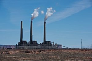 Three large smokestacks rise above a large power plant on a desert plain.